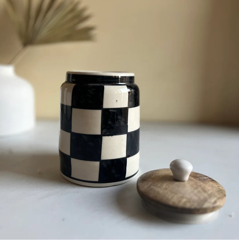 Black and white checkered jar with a wooden lid on a light surface.