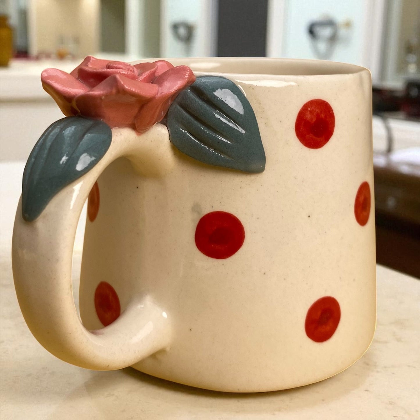 Ceramic mug with red polka dots and floral handle in a kitchen setting