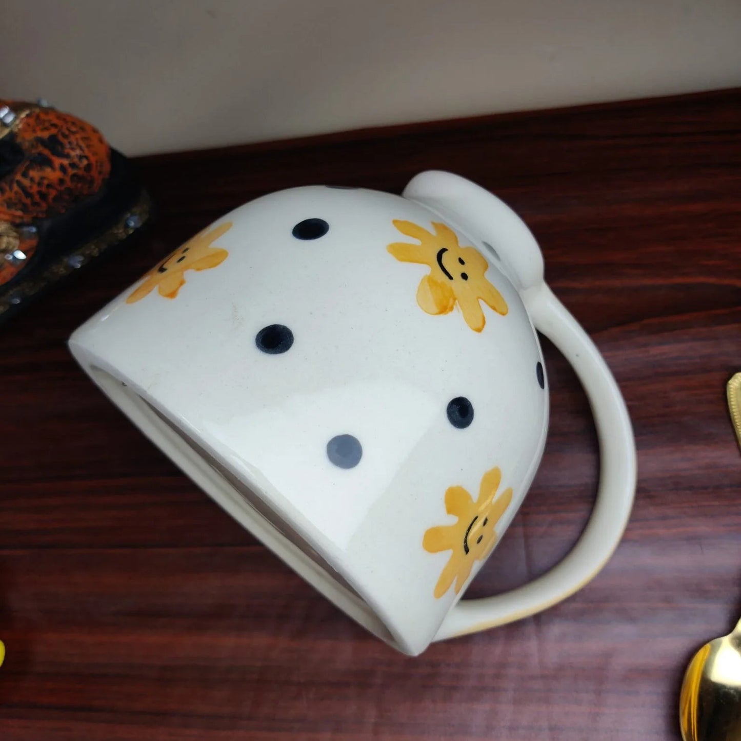 White mug with black polka dots and yellow smiley faces on a wooden surface
