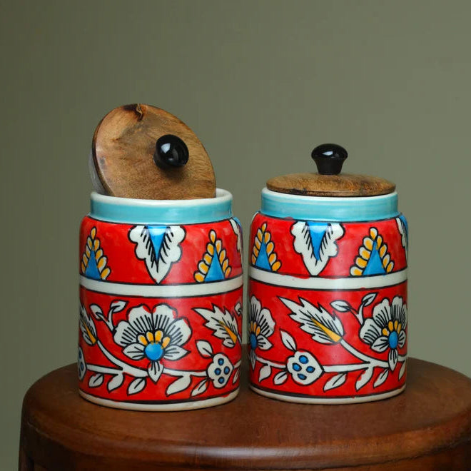 Two ceramic jars with floral patterns on a wooden surface against a plain background
