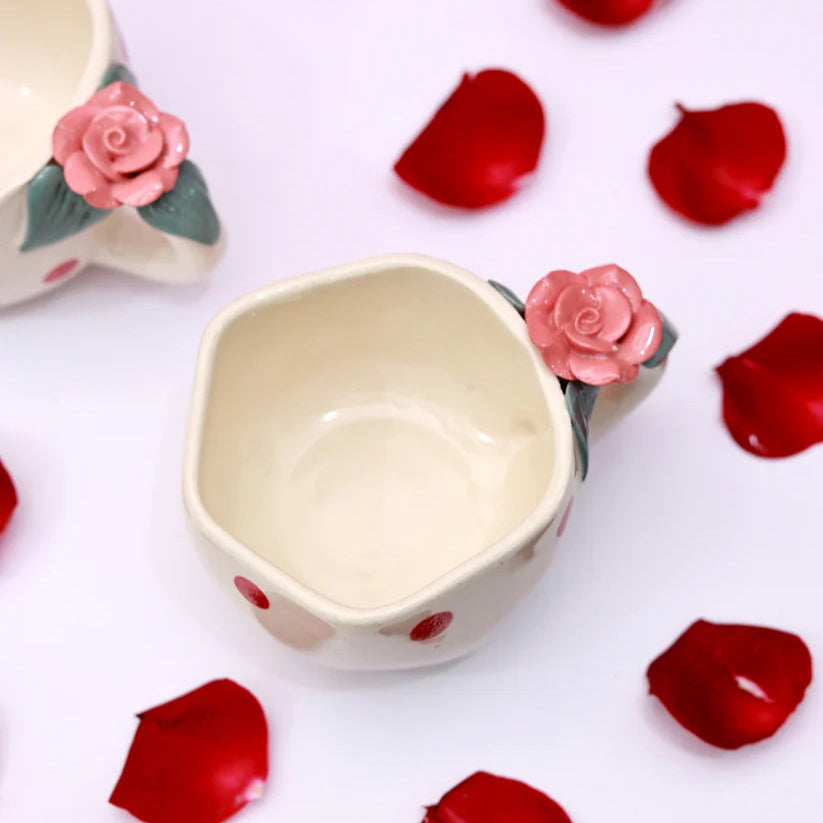 Ceramic mug with rose design on handle surrounded by red rose petals on a white background