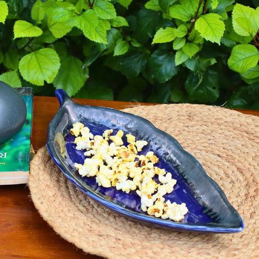 Blue leaf-shaped bowl with popcorn on a woven mat against a green leafy background