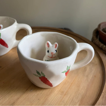 Ceramic mug with a small mouse figurine inside on a wooden surface.