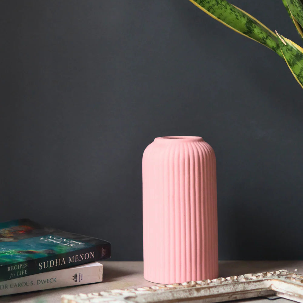 Pink textured vase on a dark surface with books and a plant leaf.
