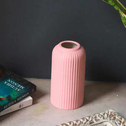 Pink ribbed vase on a surface with a dark gray wall and book in the background
