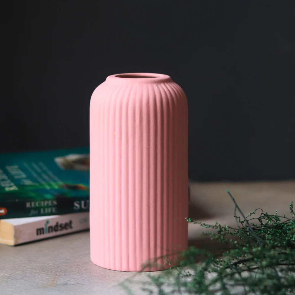 Pink ribbed vase on a surface with books and greenery in the background