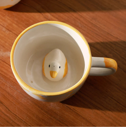 Ceramic mug with a duck-shaped figure inside on a wooden surface