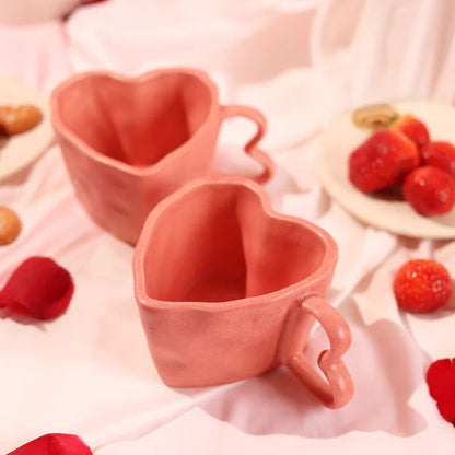 Two heart-shaped pink mugs on a soft pink fabric background with strawberries.