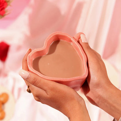 Heart-shaped pink container held by a hand against a soft pink background