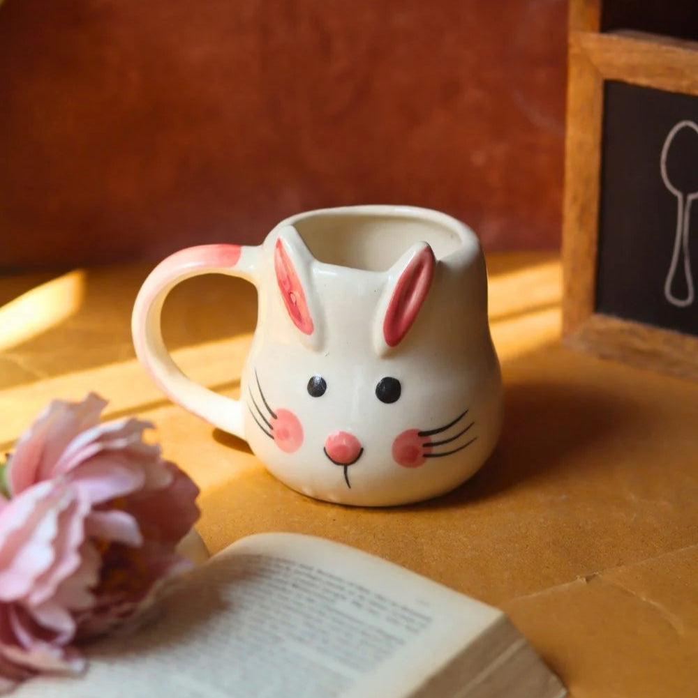Ceramic mug shaped like a rabbit with a book and flower on a wooden surface