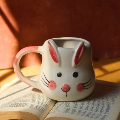 Ceramic mug shaped like a rabbit with pink ears and nose, sitting on an open book.