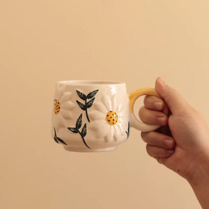 Hand holding a ceramic mug with floral design on a beige background