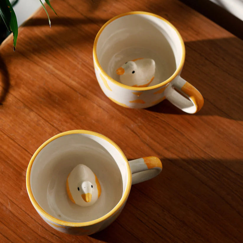 Two ceramic mugs with duck-shaped handles on a wooden surface.