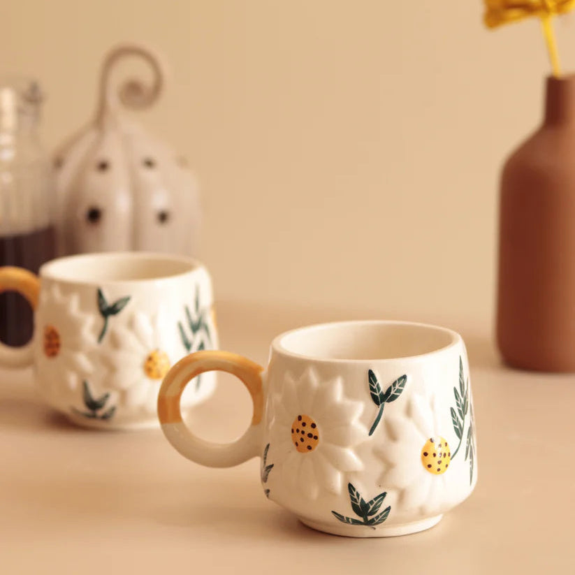 Two ceramic mugs with decorative handles on a beige surface.