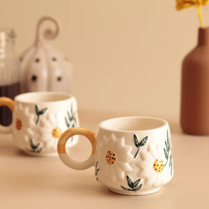 Two ceramic mugs with decorative handles on a beige surface.