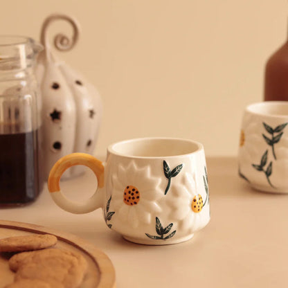 Ceramic mug with floral design on a table with cookies and a jar of coffee.