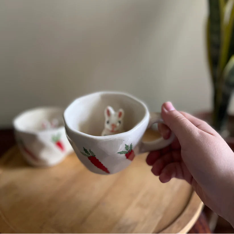 Person holding a small ceramic cup with a mouse design on a wooden surface.