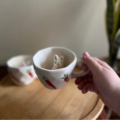 Person holding a small ceramic cup with a mouse design on a wooden surface.