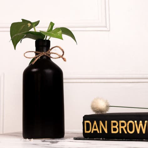 Black vase with a plant and a decorative sign reading 'Dan Brown' on a white surface.