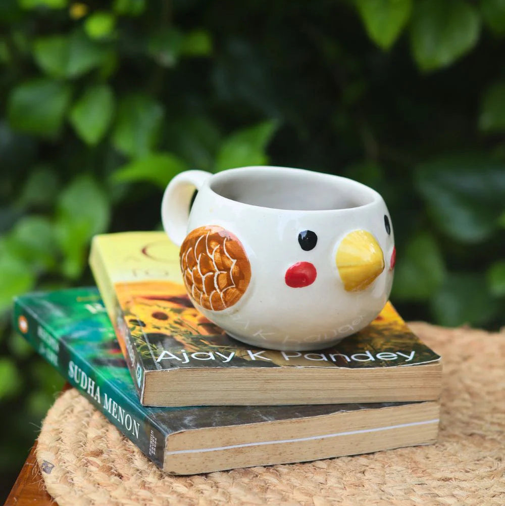 White ceramic mug with chicken design on a stack of books against a green leafy background