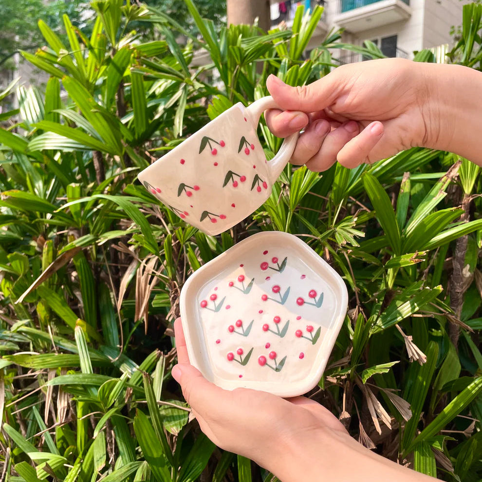 Two ceramic items with floral patterns held by a person against a green foliage background.