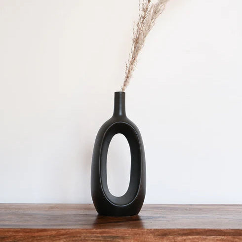 Black vase with dried plants on a wooden surface against a white wall