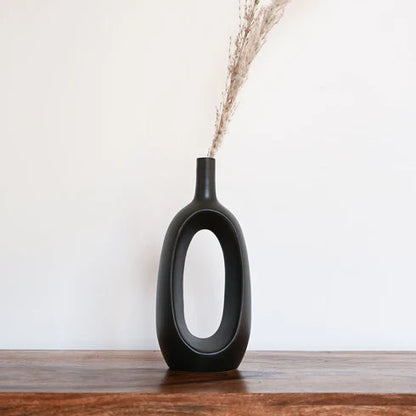 Black vase with dried plants on a wooden surface against a white wall