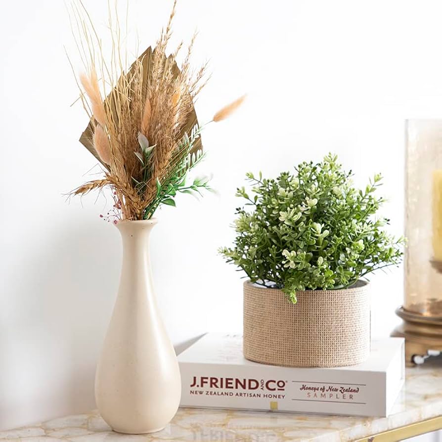 Decorative setup with a vase of dried plants and a potted plant on books.