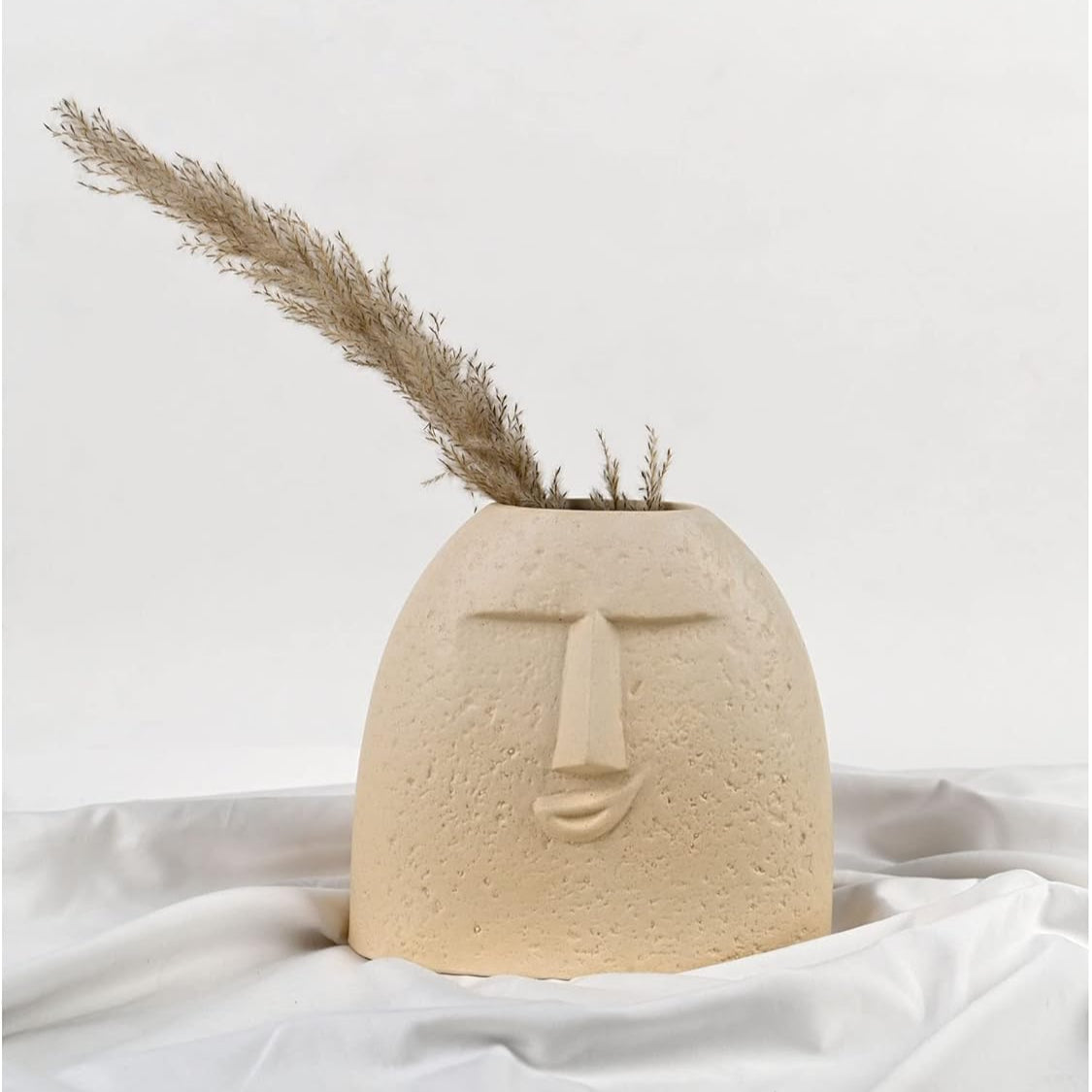 Ceramic face-shaped vase with dried plants on a white background