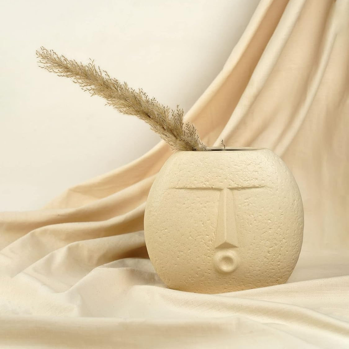 Beige ceramic vase with a face design on a beige fabric background