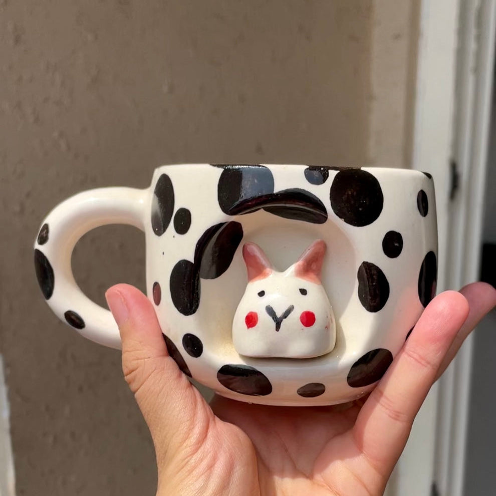 Hand holding a polka dot mug with a rabbit design