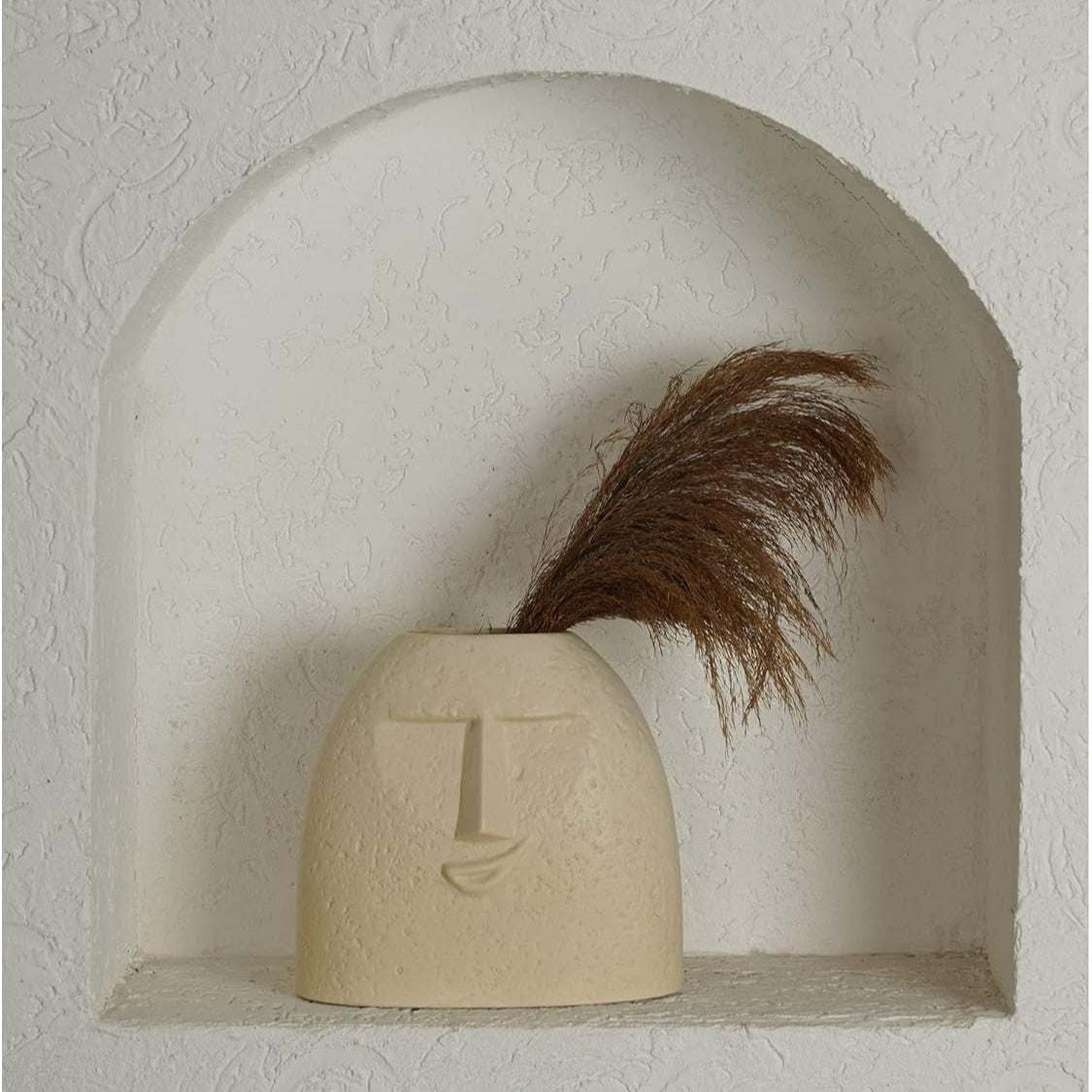 Beige ceramic vase with letter 'L' design on a textured wall shelf