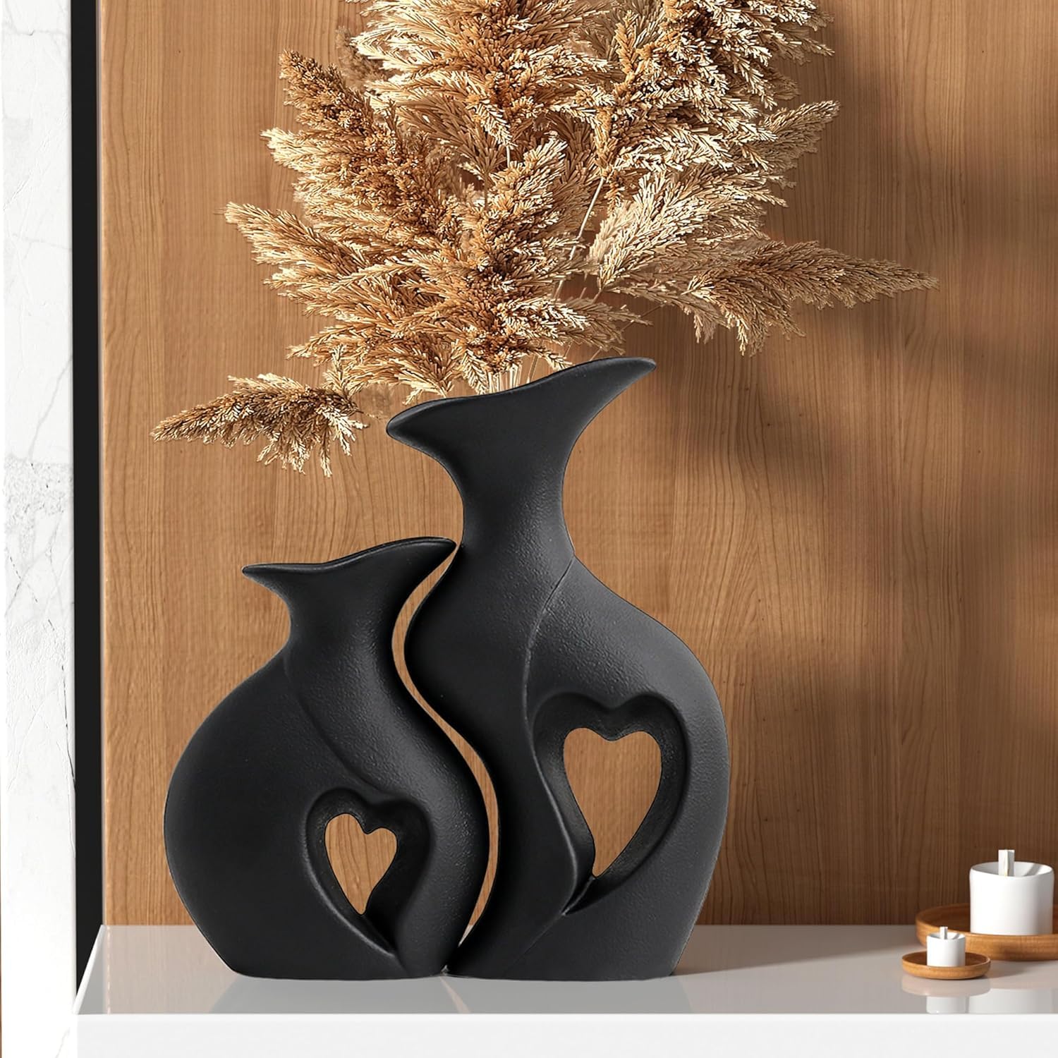 Two black ceramic vases with heart designs on a wooden surface.