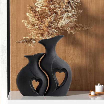 Two black ceramic vases with heart designs on a wooden surface.