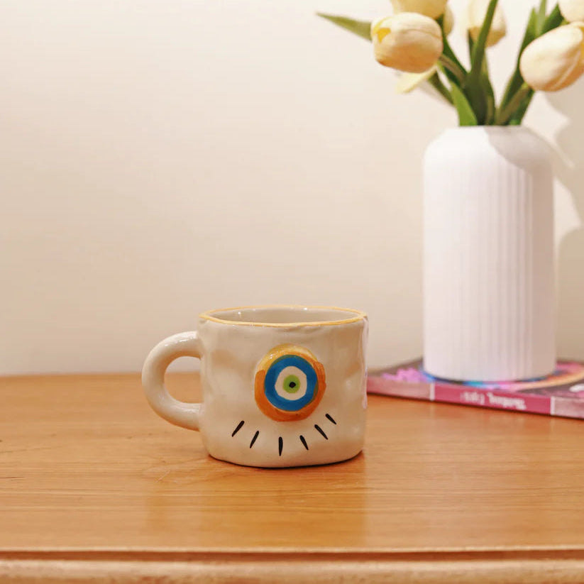 Ceramic mug with a unique design on a wooden surface next to a vase with flowers.