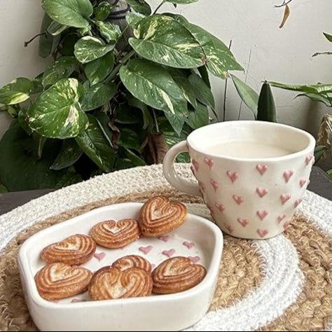 Cup with heart pattern on a woven mat with cookies, surrounded by plants
