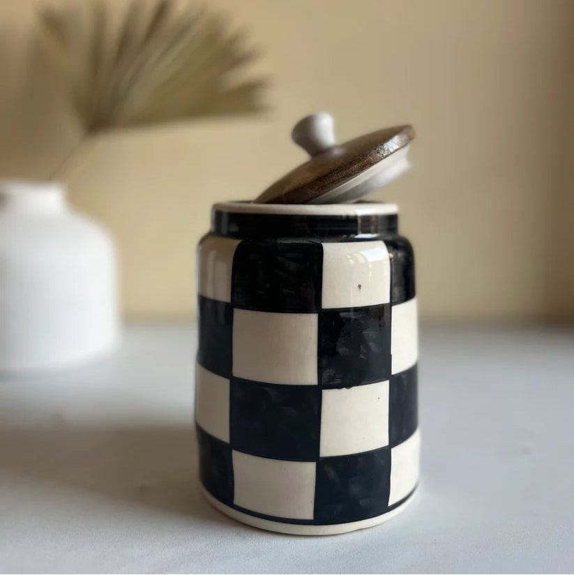 Ceramic jar with checkered pattern and wooden lid on a neutral background