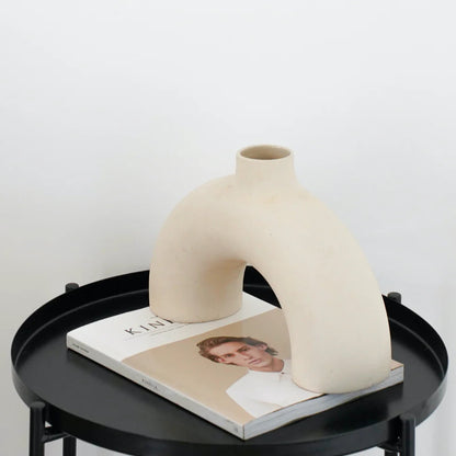 Beige ceramic vase on a black round table with a magazine underneath
