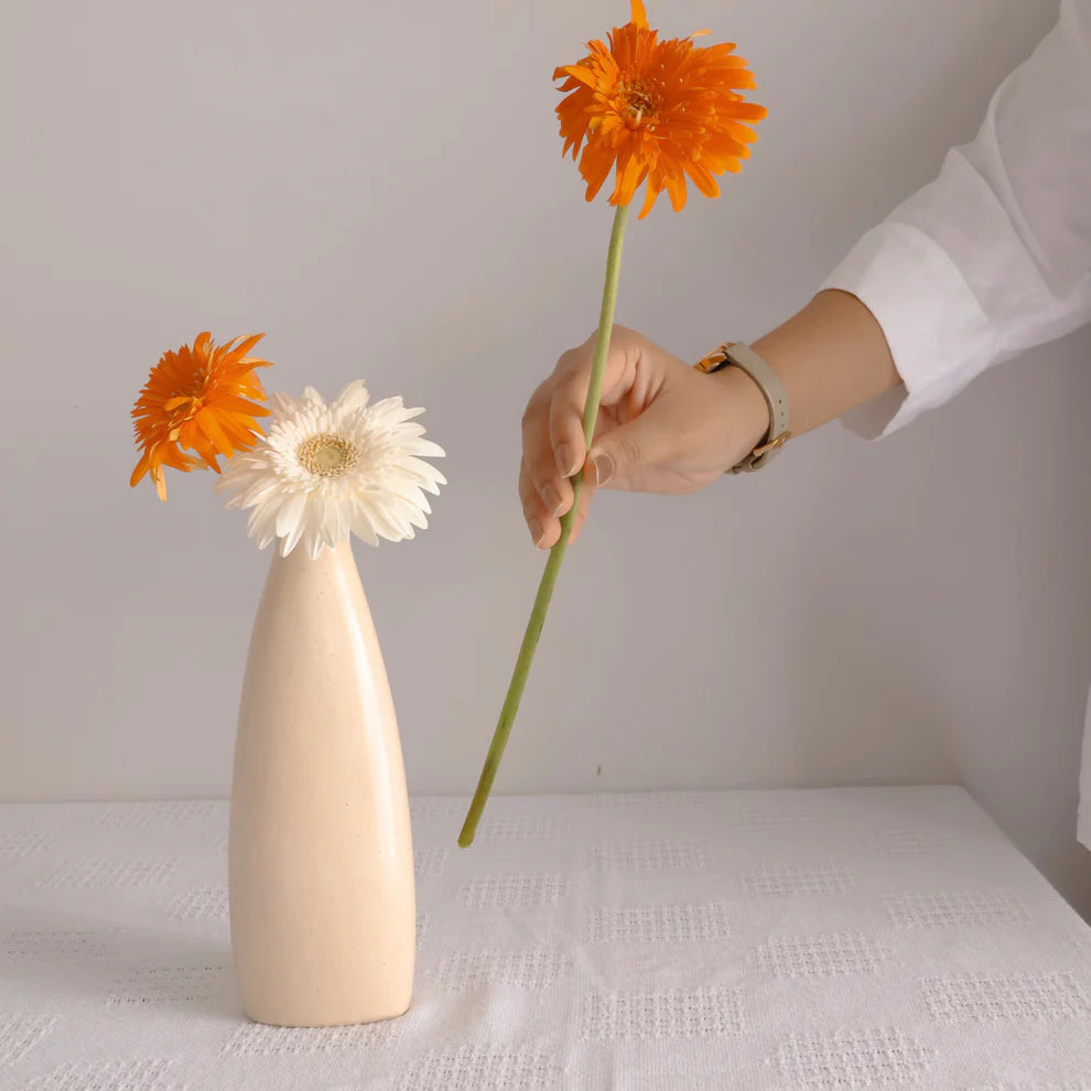 Person arranging flowers into a beige vase on a white surface.
