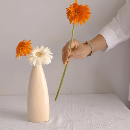 Person arranging flowers into a beige vase on a white surface.