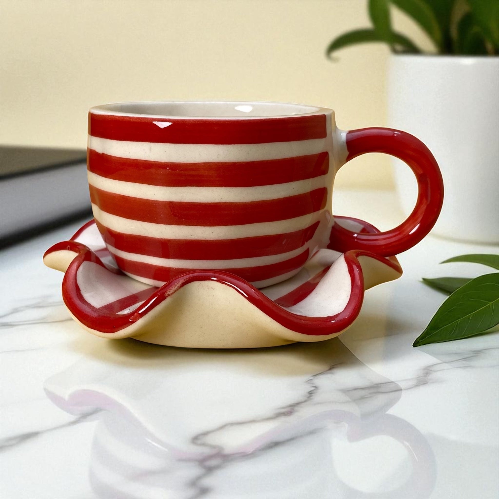 Red and white striped mug with matching saucer on a marble surface