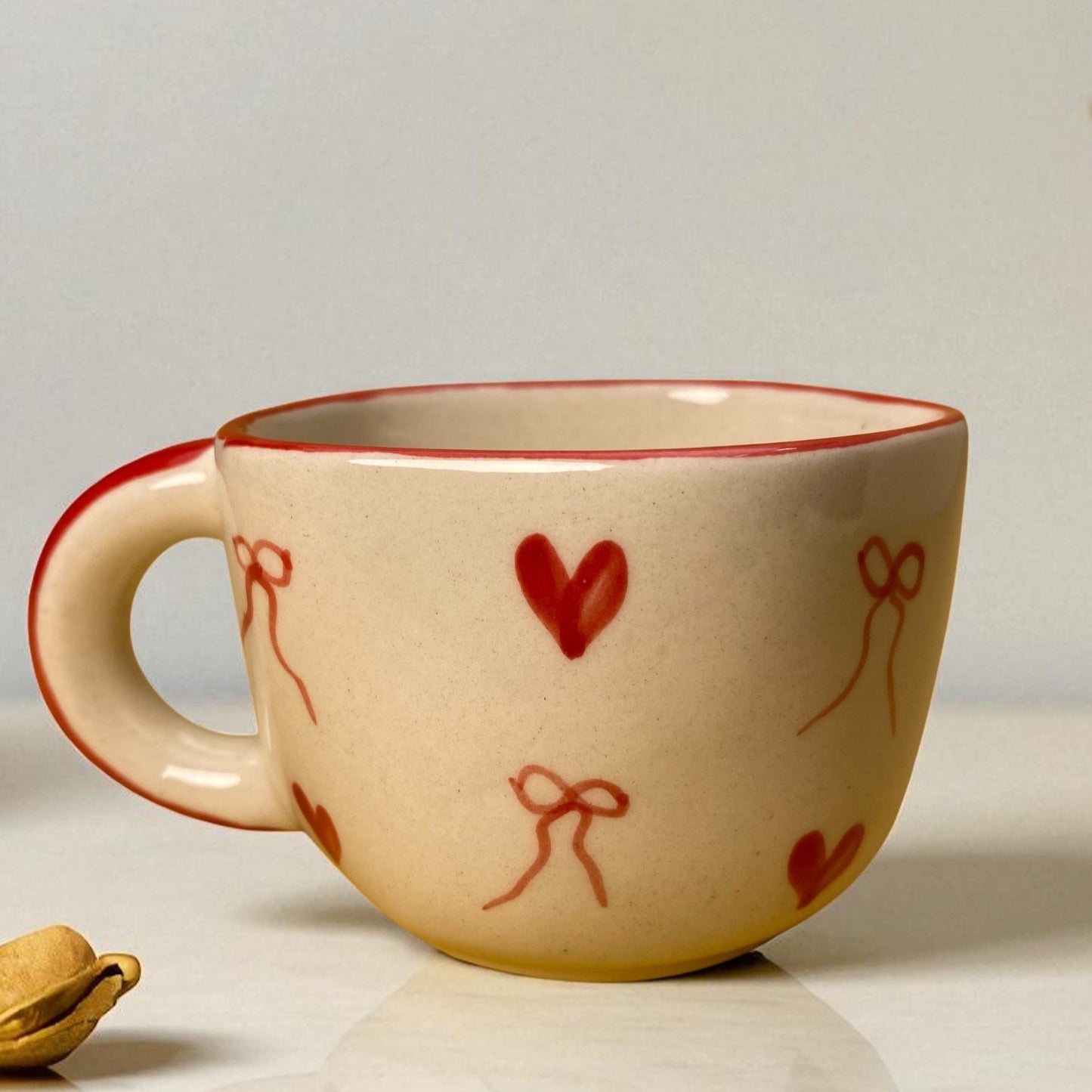 Ceramic mug with red heart and bow designs on a light surface.