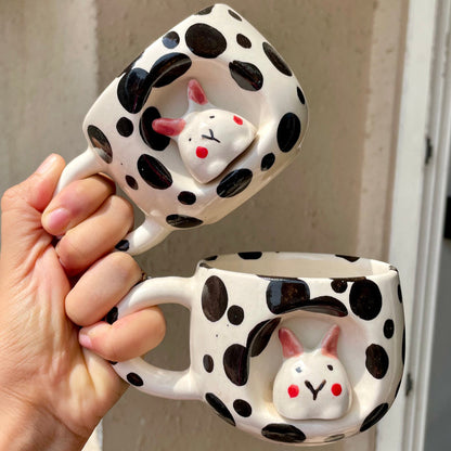 Two polka dot mugs with rabbit designs held by a hand against a neutral background