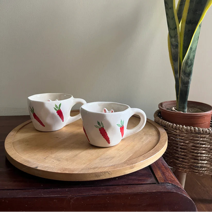 Two mugs with carrot design on a wooden tray next to a potted plant.