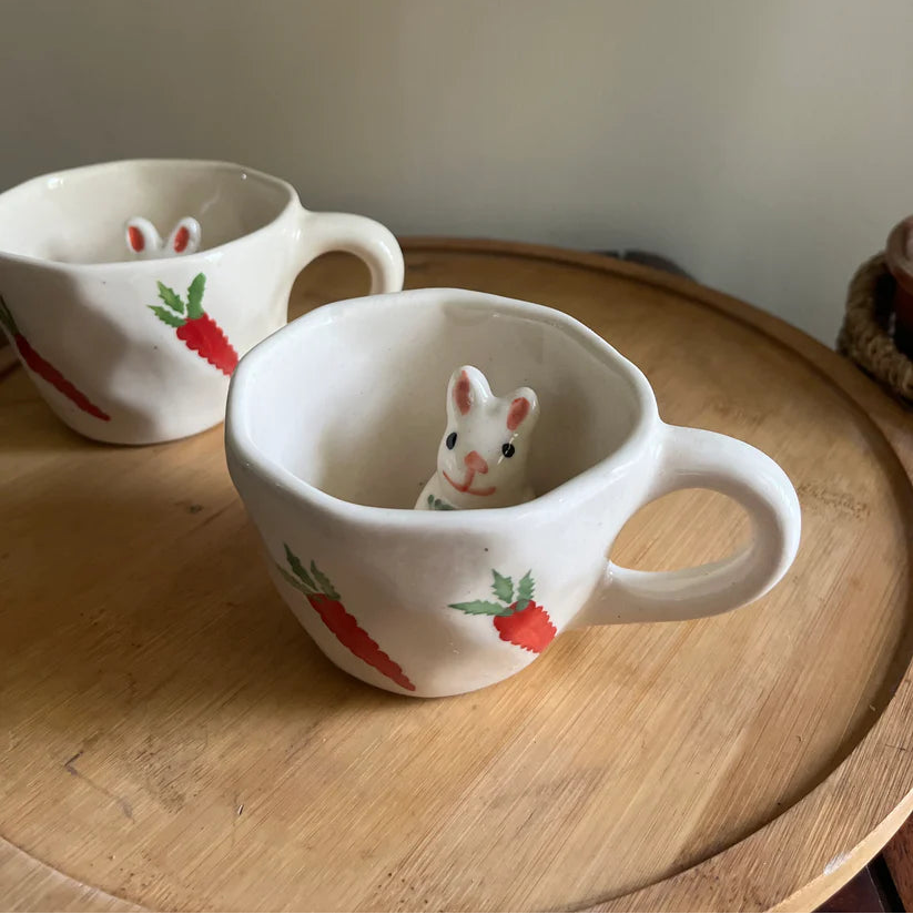 Two ceramic mugs with rabbit designs on a wooden surface.