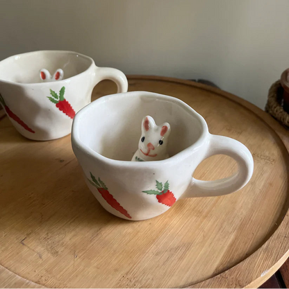 Two ceramic mugs with rabbit designs on a wooden surface.