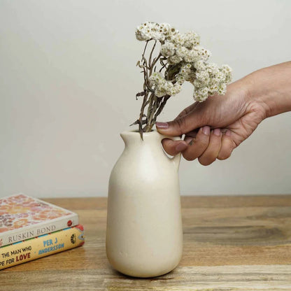 Hand placing dried flowers into a small beige vase on a wooden table.