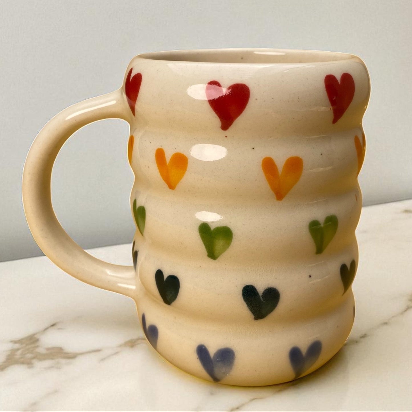 Ceramic mug with colorful heart patterns on a marble surface