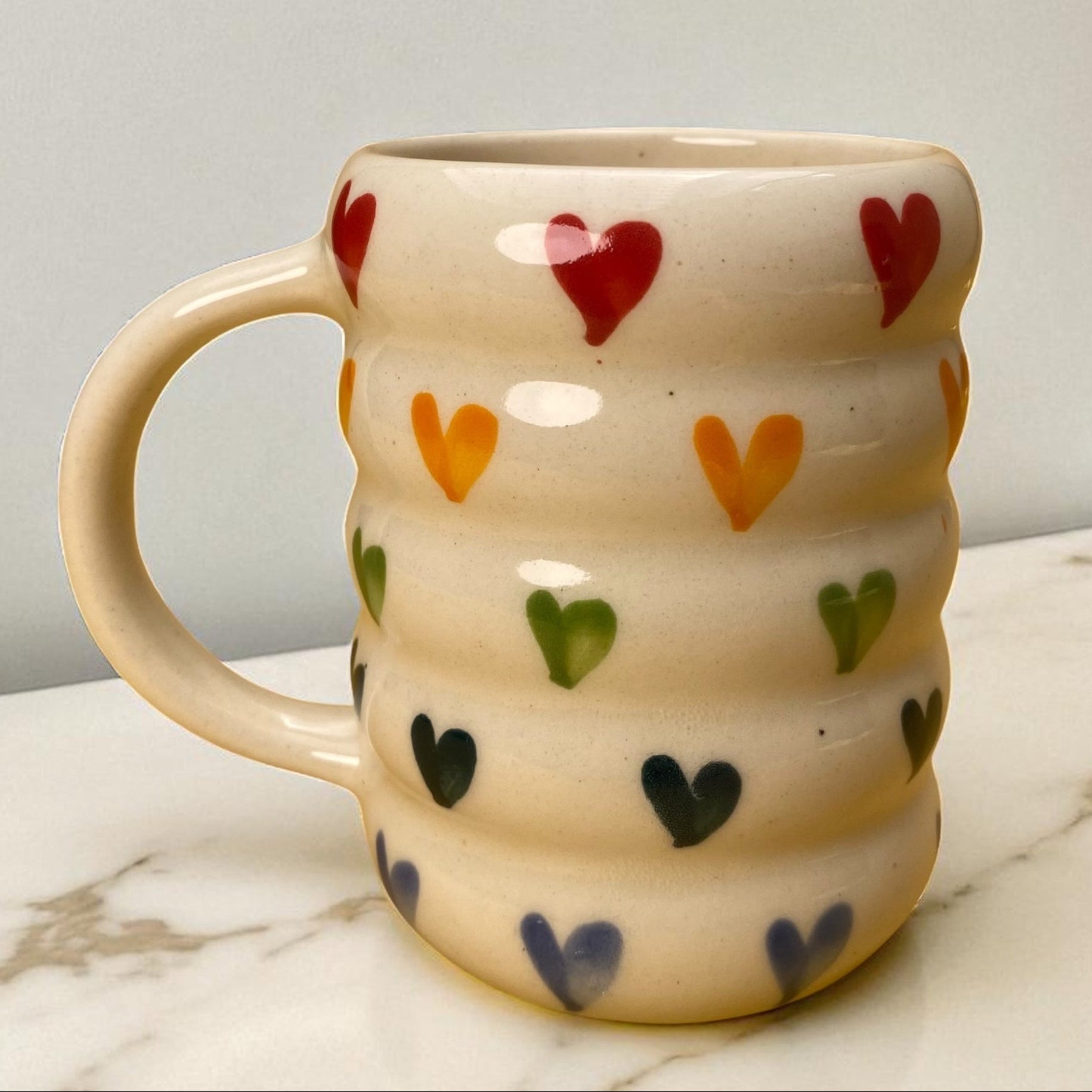 Ceramic mug with colorful heart patterns on a marble surface
