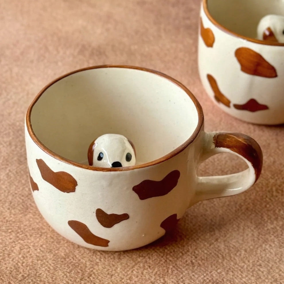 Two ceramic mugs with animal figures inside on a beige background